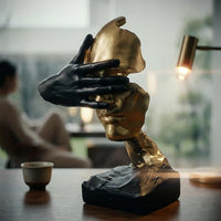 Gold abstract face sculpture arranged with books on a contemporary living room shelf