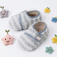 Infant wearing soft bear-themed footwear while resting on a nursery blanket.
