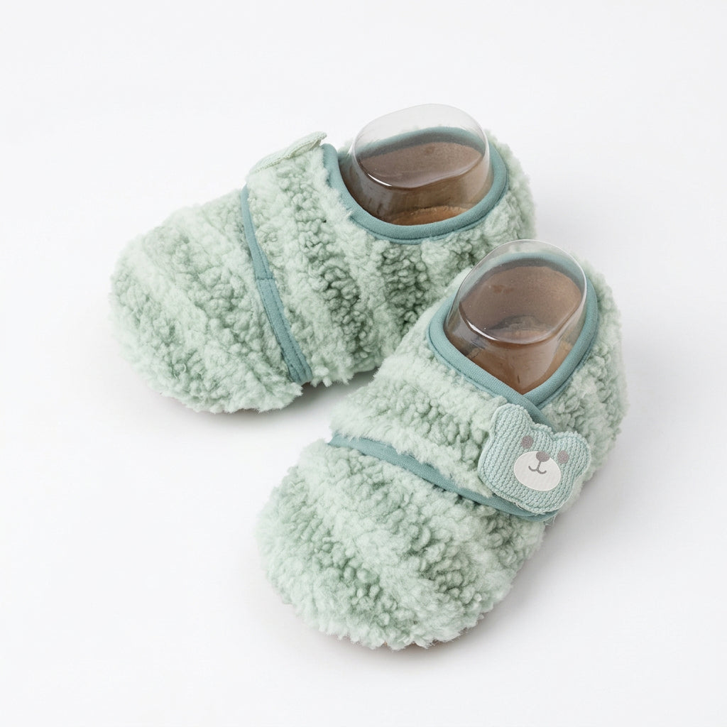 Plush newborn footwear styled beside a neutral knitted romper and baby cardigan.