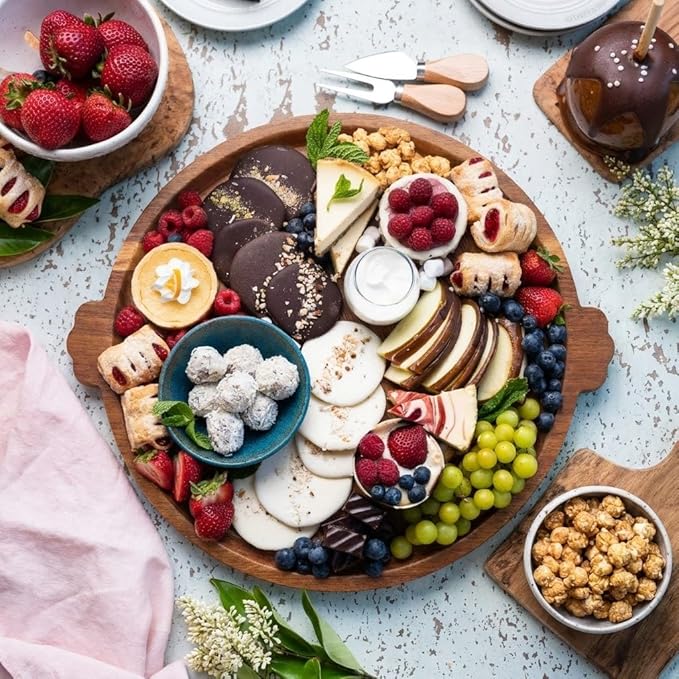 Circular wooden cheese board arranged with snacks and fruit